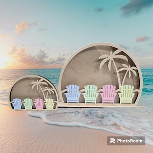 Op de afbeelding: Een houten uitsnijding van een strandsc&egrave;ne met palmbomen en vijf kleurrijke Adirondack-stoelen. De uitsnijding bevindt zich op een wit zandstrand met blauwe oceaan op de achtergrond.