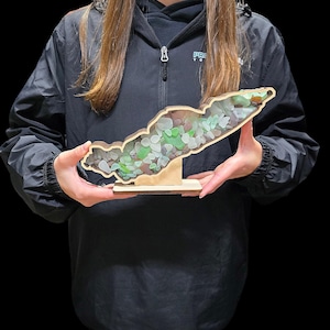 May include: A wooden cutout of an island with a stand, filled with green and white sea glass.
