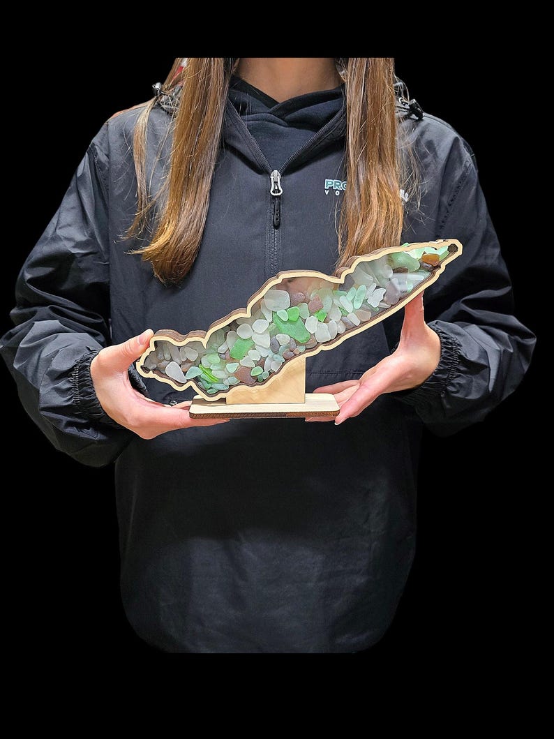 May include: A wooden cutout of an island with a stand, filled with green and white sea glass.