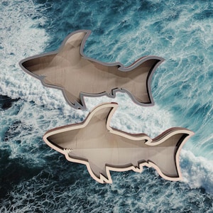 May include: Two wooden shark cookie cutters, one on top of the other, against a blue and white ocean wave background.