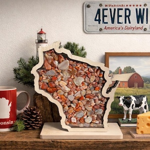May include: A wooden display case shaped like the state of Wisconsin, filled with a collection of polished, multi-colored agate stones in shades of red, orange, brown, and grey, mounted on a flat wooden base for tabletop presentation.
