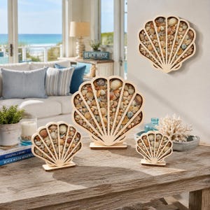 May include: A collection of four shell-shaped wooden frames filled with assorted small seashells. One frame is mounted on the wall, while three varying sizes stand on a wooden surface. The frames feature a light wood finish and radial slats.