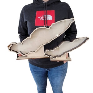 May include: A wooden cutout of the Great Lakes, with each lake individually cut out and layered. The cutout is held by a person wearing a black jacket with a red "The North Face" logo.