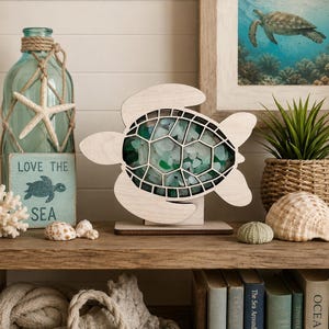May include: A light-colored wooden sea turtle cutout featuring a hollow shell filled with various shades of green and white sea glass. The turtle is mounted on a rectangular wooden base and stands upright as a decorative tabletop display piece.