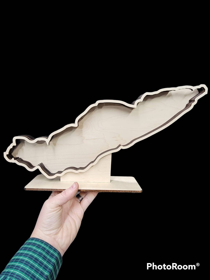 May include: A wooden cutout of an island with a brown outline and a natural wood finish. The cutout is mounted on a small wooden base.