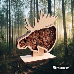 May include: Wooden moose head cutout with a base, filled with small, colorful stones. The moose head is a light brown color and the stones are a variety of reds, browns, and oranges.