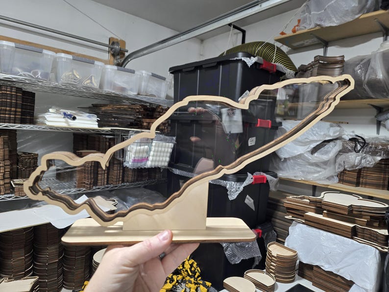 May include: A wooden cutout of a lake, with a clear acrylic insert, is displayed on a wooden base. The cutout is a detailed representation of the lake's shoreline.