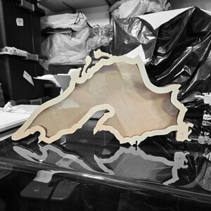 May include: A wooden cutout of Lake Superior, a large freshwater lake in North America. The cutout is light brown and has a smooth, polished finish.