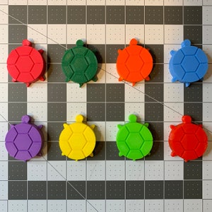 May include: Eight colorful turtle-shaped game pieces. The pieces are red, orange, yellow, green, blue, purple, and two shades of red.