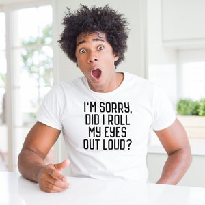 Puede incluir: Un hombre con el pelo oscuro y rizado lleva una camiseta blanca con el texto "I'm sorry, did I roll my eyes out loud?" impreso en ella. Est&aacute; mirando a la c&aacute;mara con una expresi&oacute;n de sorpresa.