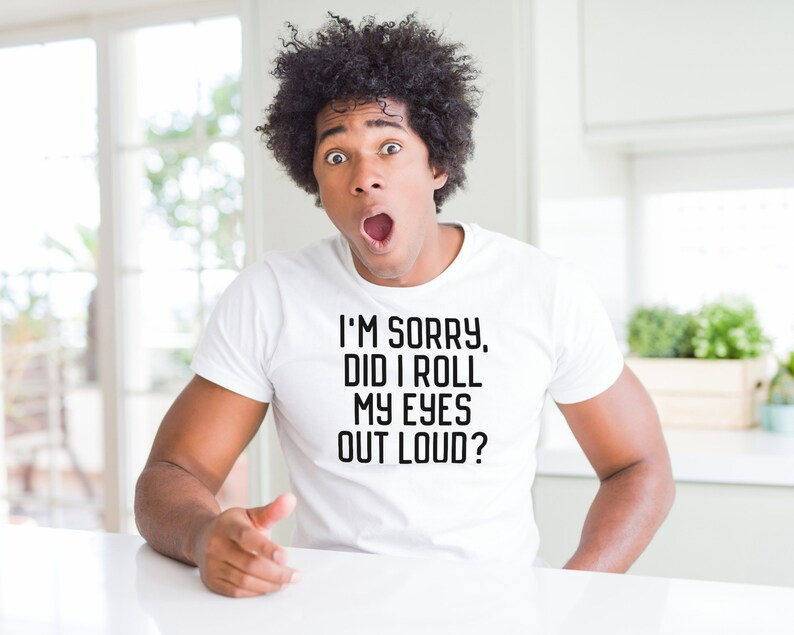 Puede incluir: Un hombre con el pelo oscuro y rizado lleva una camiseta blanca con el texto "I'm sorry, did I roll my eyes out loud?" impreso en ella. Est&aacute; mirando a la c&aacute;mara con una expresi&oacute;n de sorpresa.
