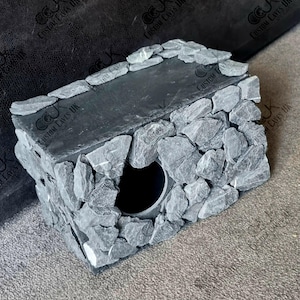 May include: A grey slate hide with a round opening, made by Custom Caves UK. The hide is made of small, irregular pieces of slate.