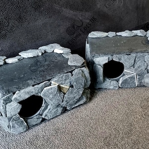 May include: Two grey stone boxes with a hole in the front. The boxes are made of small, flat stones and have a black slate top.