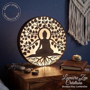 Puede incluir: Una lámpara circular de madera con la silueta retroiluminada de una figura meditando bajo un árbol con hojas y raíces detalladas. La lámpara muestra el texto "Édition Limitée Fabriqué à la Main" y "Lumière Zen Créations Boutique Etsy: LumiereZen".