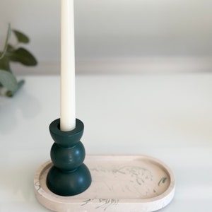 Puede incluir: Una vela blanca se encuentra en un candelero verde oscuro sobre una bandeja ovalada beige claro con un diseño de mármol verde.