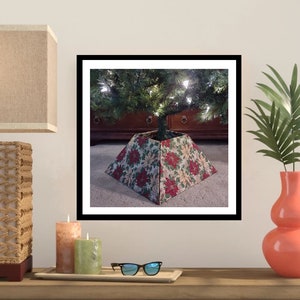 May include: A Christmas tree skirt with a poinsettia pattern in shades of red, green, and white. The skirt is made of fabric and has a square shape.