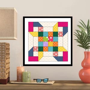 May include: A framed quilt block with a colorful patchwork design. The quilt features squares of pink, blue, yellow, green, and orange fabrics. The quilt is framed in a black frame and is displayed on a wooden surface.