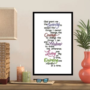 May include: A framed print with the text "God grant me the Serenity..." in various colors. The print is displayed on a wooden surface with candles, a tray, and eyeglasses. A lamp and a vase with a plant are also visible.