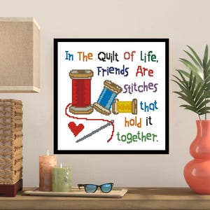 Puede incluir: Imagen de punto de cruz con el texto "In The Quilt Of Life, Friends Are Stitches That Hold It Together." Presenta carretes de hilo rojo, azul y amarillo, un corazón rojo y una aguja. Enmarcado en negro.
