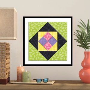 Puede incluir: Una impresión enmarcada de un bloque de colcha colorido con un diseño geométrico. El bloque de colcha está hecho de cuadrados en tonos de rosa, amarillo, morado, negro y verde. El fondo es una tela verde con un patrón de hojas.