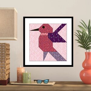 May include: A framed print of a colorful patchwork hummingbird with pink, purple, and blue fabric pieces. The background is a light pink with a subtle pattern.