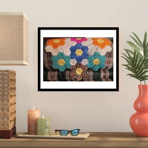 May include: A colorful quilt with a hexagonal flower pattern in shades of blue, yellow, orange, pink, and white. The quilt is displayed on a couch with a plaid fabric.
