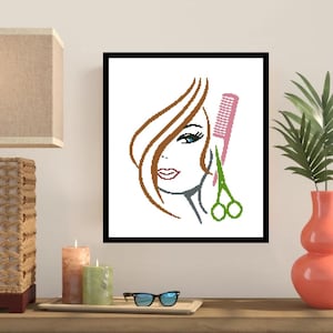 May include: A framed artwork featuring a stylized illustration of a woman's face with brown hair, blue eyes, and red lips. A pink comb and green scissors are positioned next to the woman's face, suggesting a salon theme.