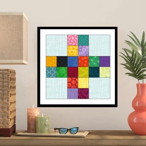 May include: A framed quilt art piece with a black frame. The quilt design features a cross shape with colorful squares of various patterns and textures. The background is a light blue fabric with a subtle white crosshatch pattern.
