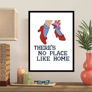 Puede incluir: Un diseño de punto de cruz enmarcado en blanco con un par de zapatos rojos con calcetines azules y una estrella rosa. El texto "There's no place like home" está escrito debajo de los zapatos.