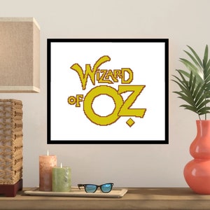 May include: A framed cross-stitch design featuring the yellow text "Wizard of Oz" with a stylized "O" in a circle.