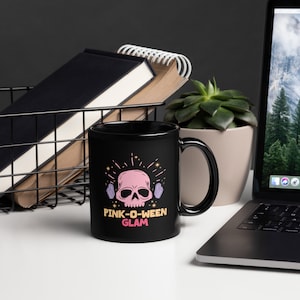 Pode incluir: Caneca de café preta com uma caveira rosa e cristais roxos, com o texto "PINK-O-WEEN GLAM" em letras rosa e pretas.