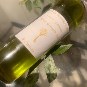 May include: A clear glass bottle with a white label that reads "Kiki's Beauty Keys", "Curry Leaves", "Hair Growth Oil", and "8 Ounces". The bottle is filled with a green liquid.
