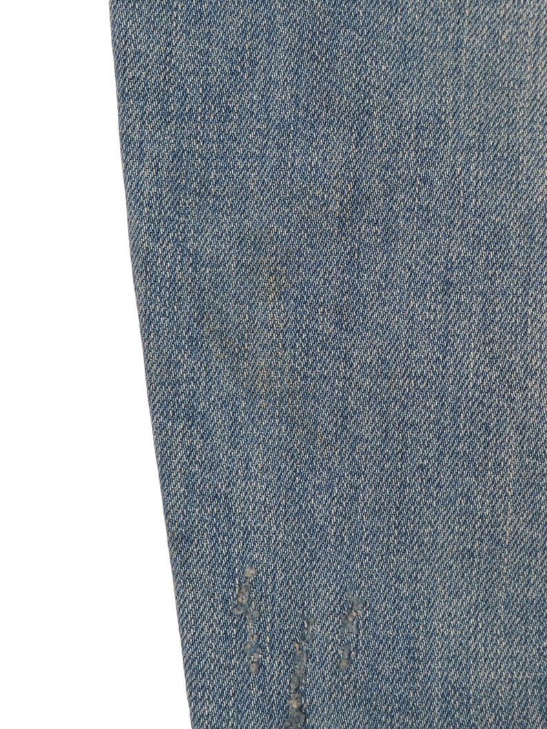 May include: Close-up of blue denim fabric with a distressed look. The fabric has a subtle texture and a faded appearance.
