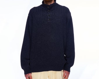 Könnte beinhalten: Ein marineblauer Strickpullover mit Rippstruktur und Knopfkragen. Der Pullover hat lange Ärmel und eine lockere Passform. Die Knöpfe sind dunkelbraun. Die Person auf dem Bild trägt eine hellgelbe Hose.