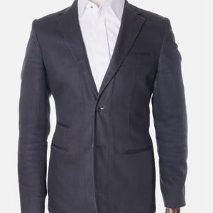 May include: A dark gray blazer with a white collared shirt underneath, displayed on a mannequin. The blazer has a two-button closure and a notched lapel. The jacket has two front pockets and a chest pocket.