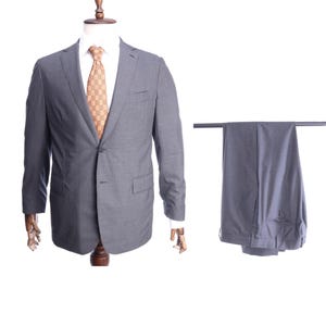 Peut inclure: Une veste de costume grise et un pantalon assorti. La veste est sur un mannequin et porte une cravate à carreaux brun et blanc.