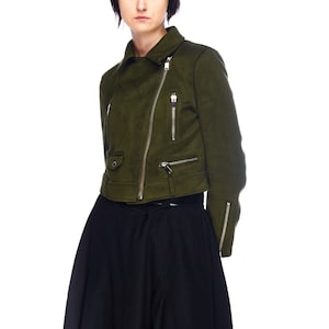 May include: A green suede jacket with a zipper closure and multiple pockets. The jacket has a cropped length and a slightly fitted silhouette.
