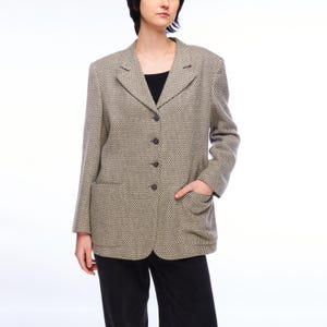 Puede incluir: Un blazer con estampado beige y negro con solapas, tres botones y dos bolsillos delanteros. El blazer se lleva sobre una camiseta negra y se combina con pantalones negros. La chaqueta tiene un diseño clásico y a medida.