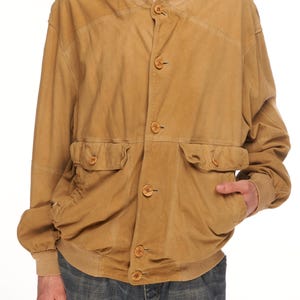 May include: A tan suede bomber jacket with a button front closure and two flap pockets. The jacket has a ribbed knit collar, cuffs, and hem.