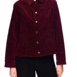 Può includere: Giacca in velluto a coste bordeaux con colletto e bottoni dorati. La giacca ha maniche lunghe e una vestibilità su misura. La modella indossa pantaloni neri.