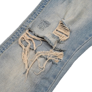 May include: Close-up of a pair of light blue denim jeans with a large distressed hole and frayed edges.