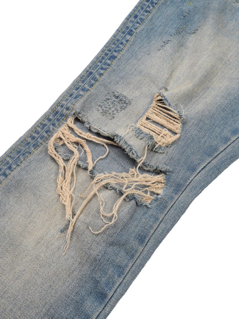 May include: Close-up of a pair of light blue denim jeans with a large distressed hole and frayed edges.