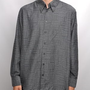 May include: A long-sleeved button-down shirt in a dark gray color with a repeating pattern of the word "VERSACE" in a lighter gray color.
