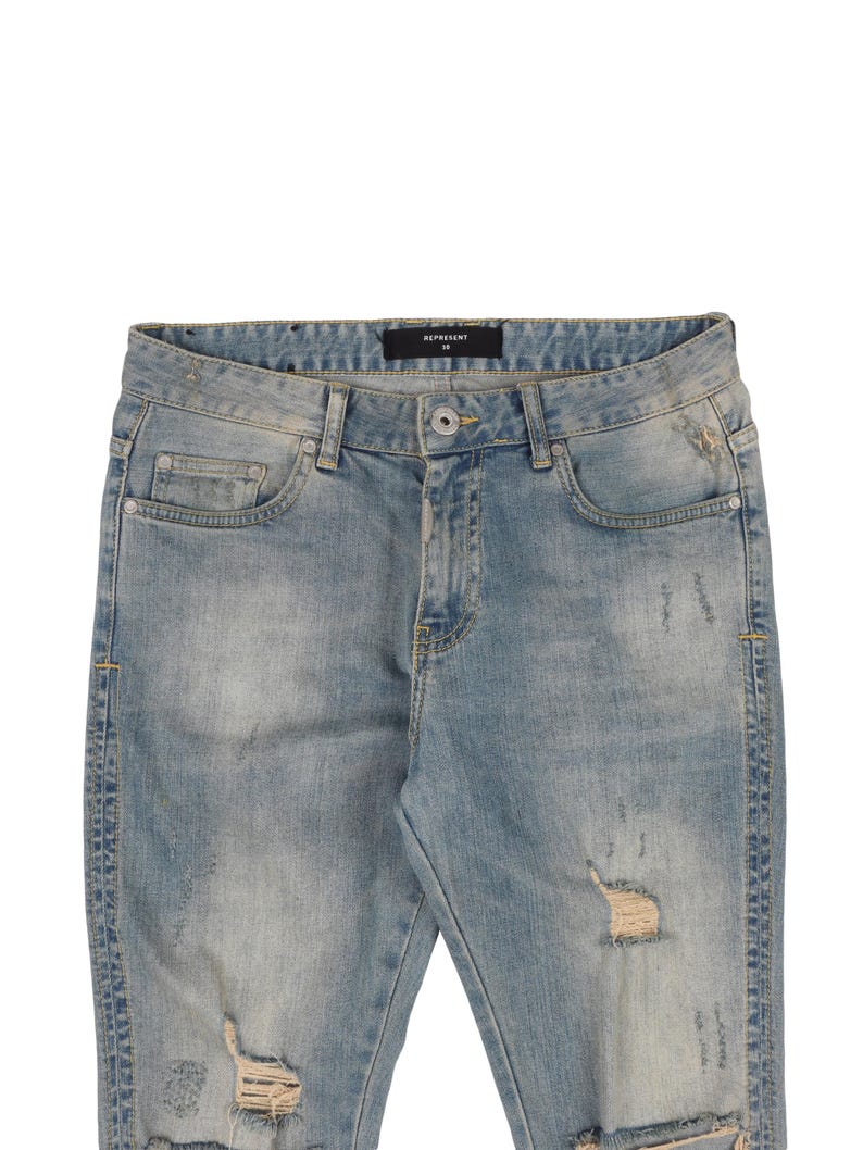 May include: Light blue distressed denim jeans with rips and tears throughout. The jeans have a black label with the text "REPRESENT" on the waistband.