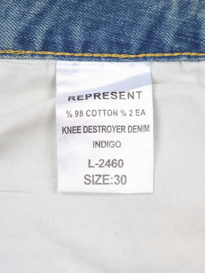 May include: A white tag with black text that reads "REPRESENT % 98 COTTON % 2 EA KNEE DESTROYER DENIM INDIGO L-2460 SIZE:30"