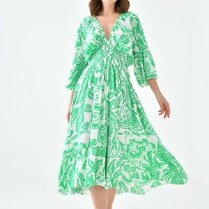 Puede incluir: Un vestido midi blanco con estampado floral verde. El vestido tiene un escote en V, mangas 3/4 y una cintura ajustada. La modelo lleva sandalias blancas.