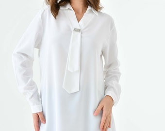 Oversized witte tuniektop met brochedetail: chic shirt met lange mouwen