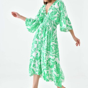 Puede incluir: Un vestido midi de estampado floral blanco y verde con escote en V y mangas 3/4. El vestido tiene una cintura fruncida y una falda fluida.