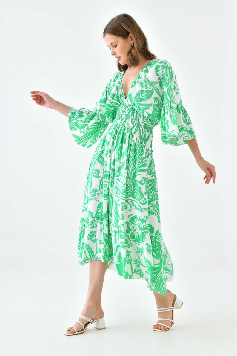 Puede incluir: Un vestido midi de estampado floral blanco y verde con escote en V y mangas 3/4. El vestido tiene una cintura fruncida y una falda fluida.