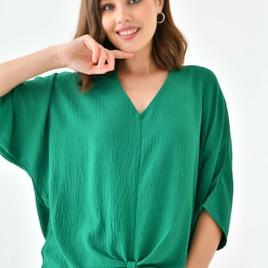 May include: A green, short-sleeved, v-neck blouse with a knotted front. The blouse is made of a textured fabric.